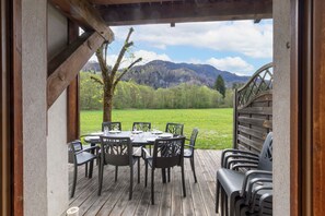 An outdoor dining area with a table and chairs, a wooden deck, and a view of a mountain landscape. - Chalet 'Triplex with Pool - Sauna' with Mountain View, Private Pool and Private Terrace (Samoëns)