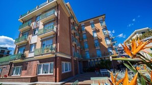 A multi-story residential building with balconies, a paved courtyard, and a clear blue sky. - Albergo Regina Mundi (Pietra Ligure)