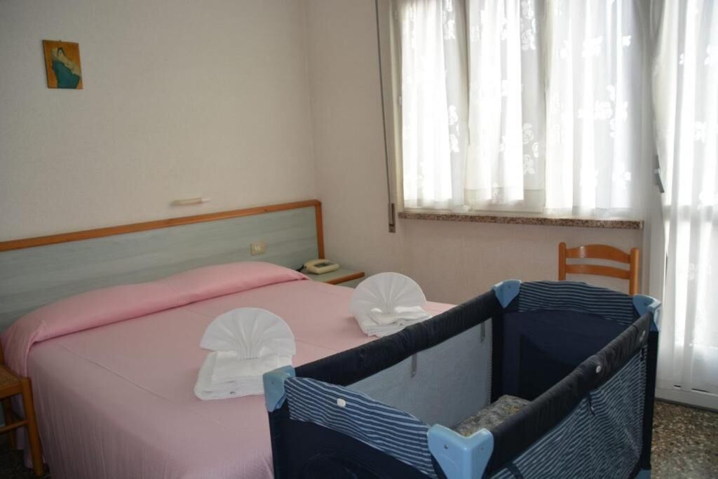 Una camera da letto con un letto, una culla, un comodino e una finestra con tende.
