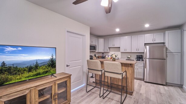 Una cocina moderna con armarios blancos, un refrigerador de acero inoxidable y una isla de madera con taburetes de bar.