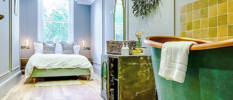 A bedroom with a bed, a green bathtub, and a window with natural light.