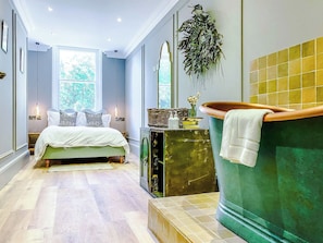 A bedroom with a bed, a green bathtub, and a window with natural light.