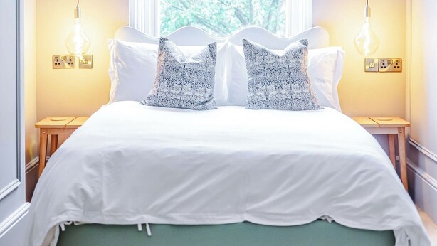 Quarto com cama, duas luminárias de cabeceira, janela com vista para árvores e mesa de cabeceira.