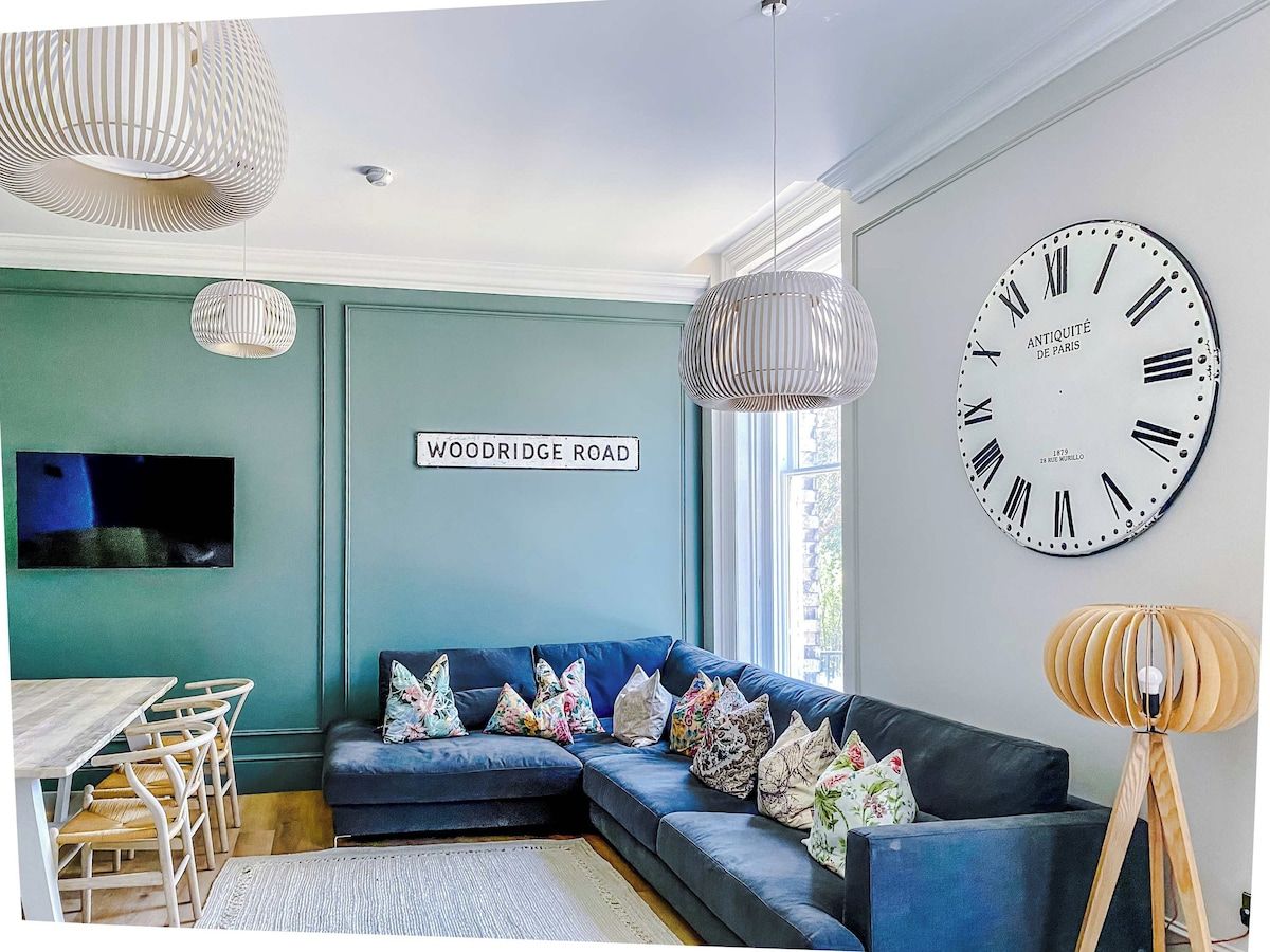 A modern living room with a blue sofa, a large wall clock, and a television mounted on the wall.
