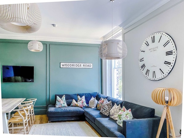 A modern living room with a blue sofa, a large wall clock, and a television mounted on the wall.