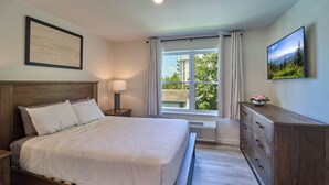 Une chambre à coucher avec un lit en bois, une table de chevet, une commode, une fenêtre avec des rideaux et un tableau encadré accroché au mur.