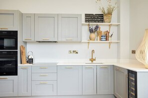 Una cocina moderna con armarios de color gris claro, un horno negro, encimera blanca y grifo dorado.