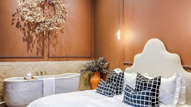 Quarto com cama grande, banheira e luminária fixada na parede.