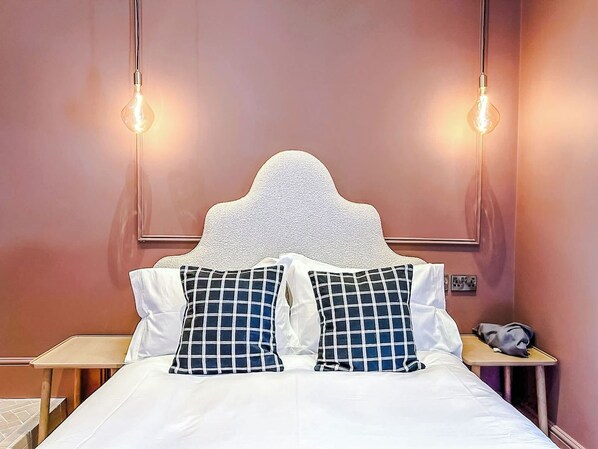 A bed with a white headboard, two pillows with a checkered pattern, and two wall-mounted light fixtures.