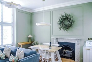 A dining area with a wooden table and chairs, a fireplace, and a green wreath on the wall.