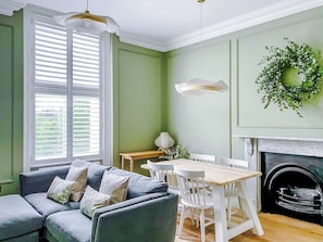 A room with a green wall, white furniture, a fireplace, and a window with shutters. - Railway House -Platform 5, 1 Bedroom Apartment. (York)