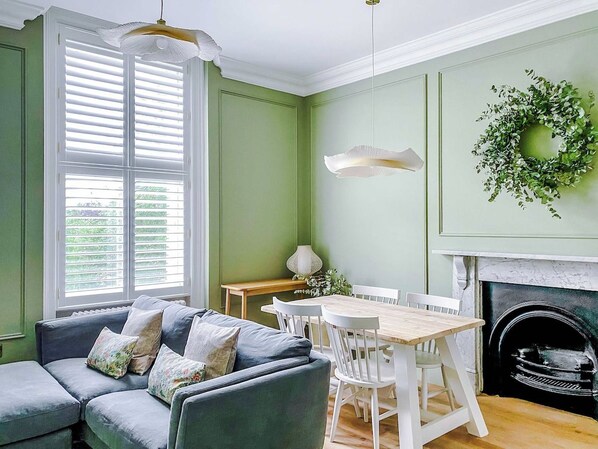A room with a green wall, white furniture, a fireplace, and a window with shutters. - Railway House -Platform 5, 1 Bedroom Apartment. (York)