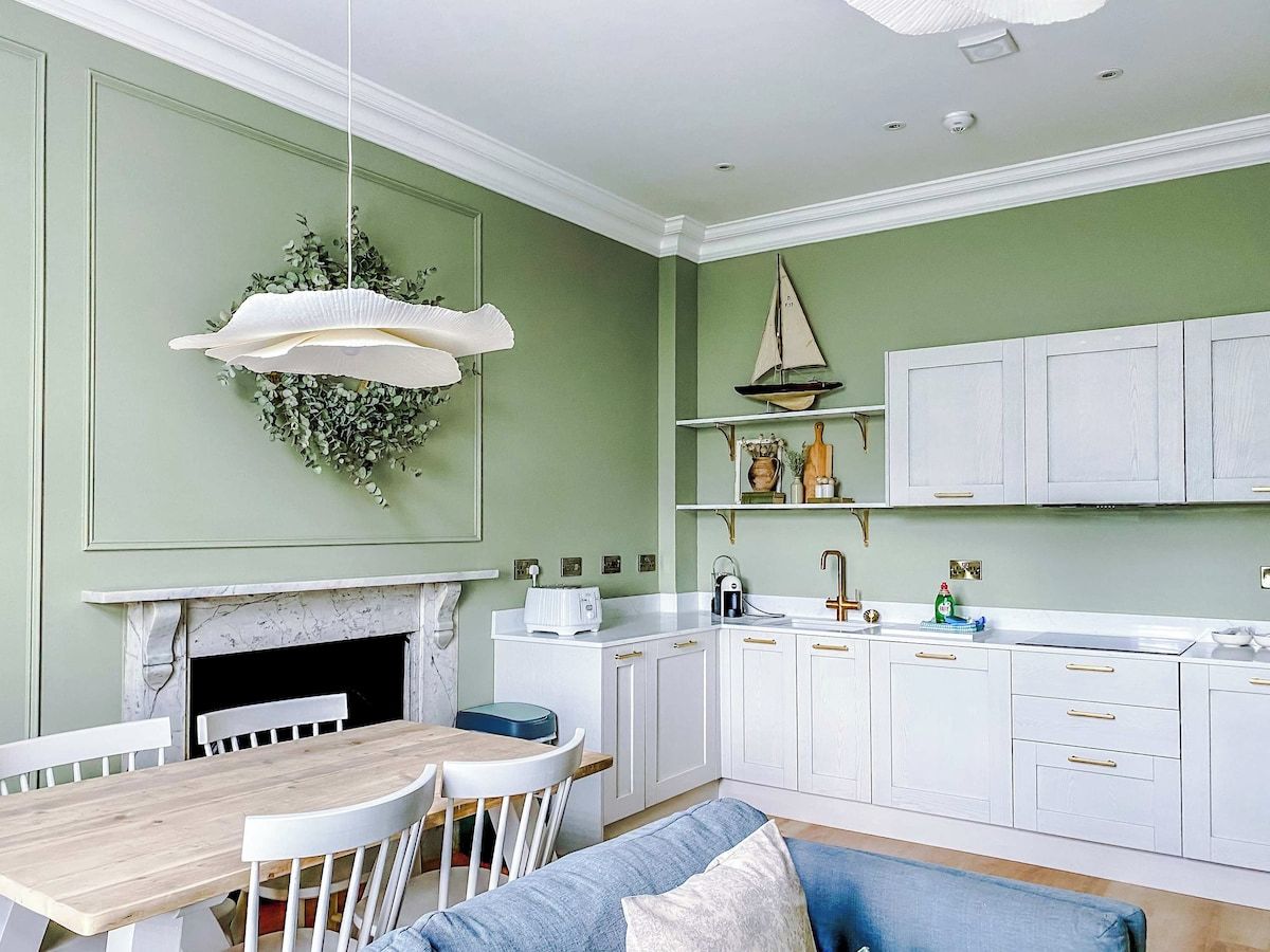 A kitchen with white cabinets, a wooden dining table, and a hanging light fixture.