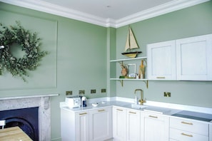 A kitchen with white cabinets, a white countertop, a built-in stove, and a wall-mounted shelf with decorative items. - Railway House -Platform 5, 1 Bedroom Apartment. (York)