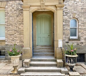 A building entrance with a green door, steps leading up to it, and two large planters with flowers. - Railway House -Platform 8, 2 Bedroom Apartment. (York)
