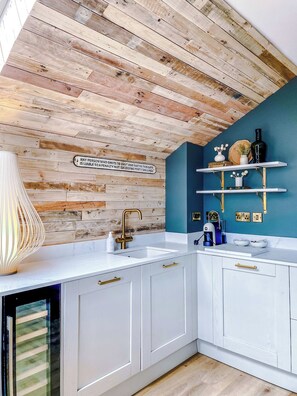 A kitchen with a wooden ceiling, white cabinets, a sink, and a blue accent wall.