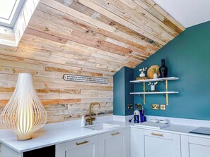 A kitchen with a wooden ceiling, white cabinets, a white countertop, a gold faucet, and a decorative lamp. - Railway House -Platform 8, 2 Bedroom Apartment. (York)