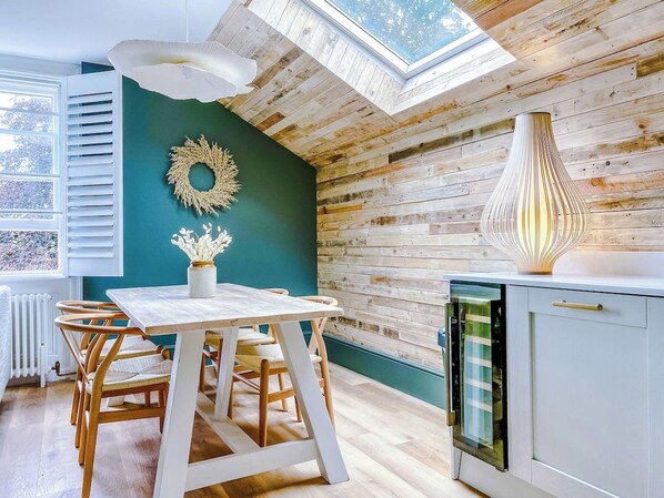 A modern kitchen with a wooden ceiling, a dining table with chairs, and a view of the outdoors through a skylight.