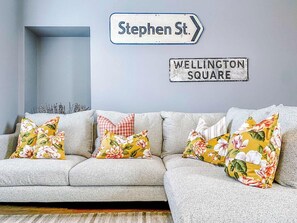 A grey sofa with floral cushions, a directional sign for Stephen St., and a sign for Wellington Square.
