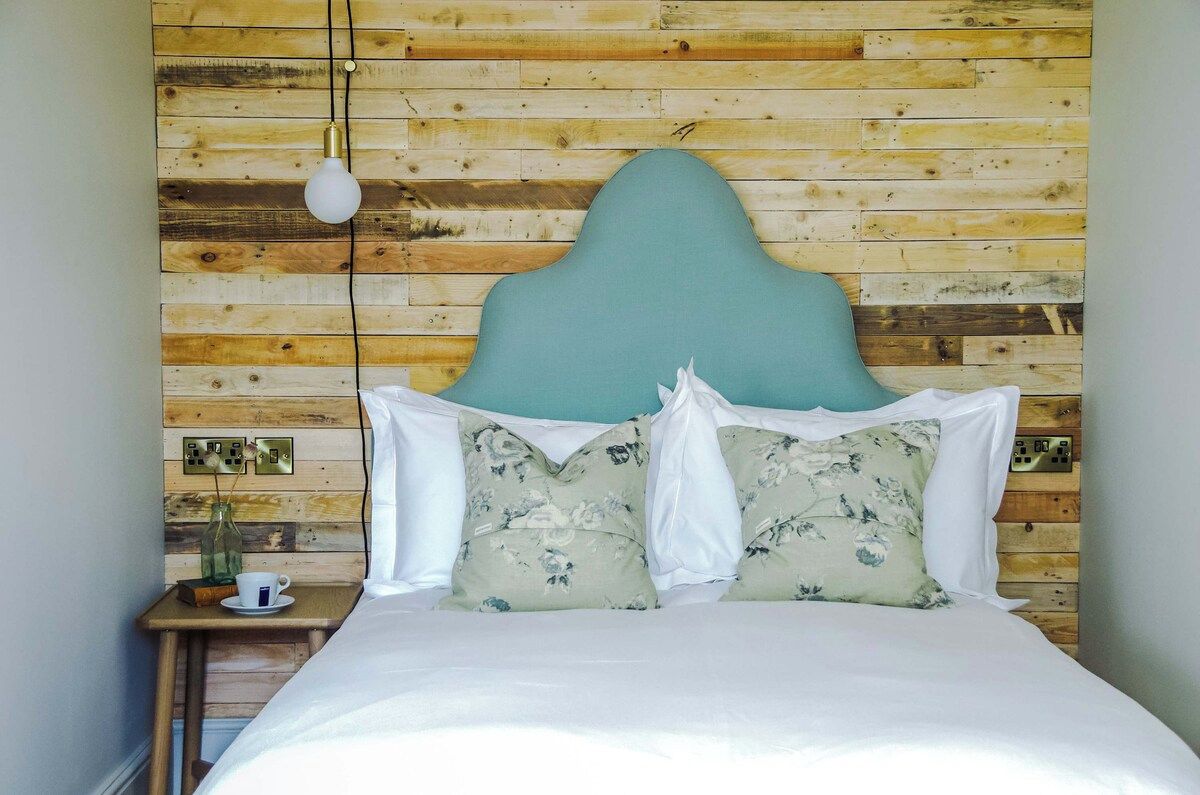A bed with a wooden headboard against a wall with electrical outlets.