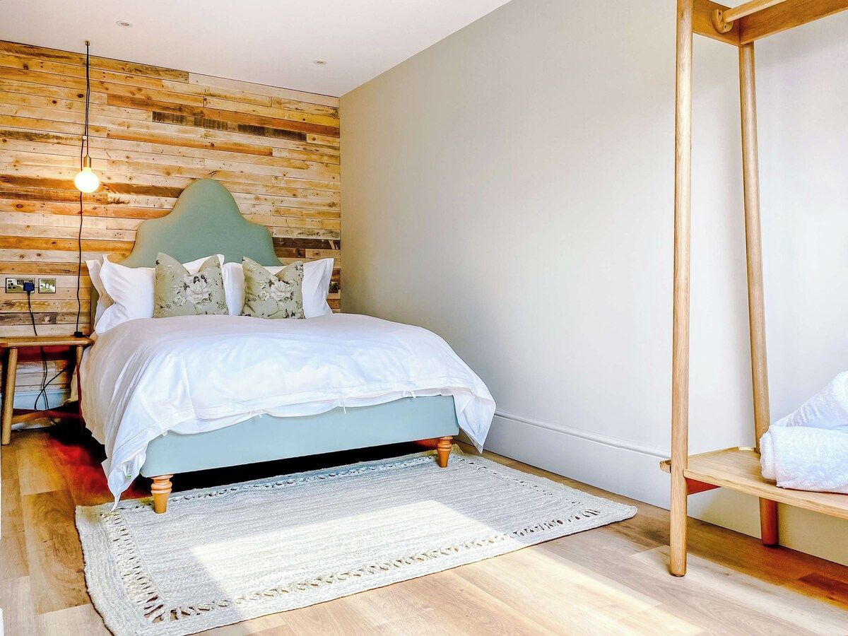 A bedroom with a bed, a wooden headboard, a bedside table, a hanging light, and a wooden floor.