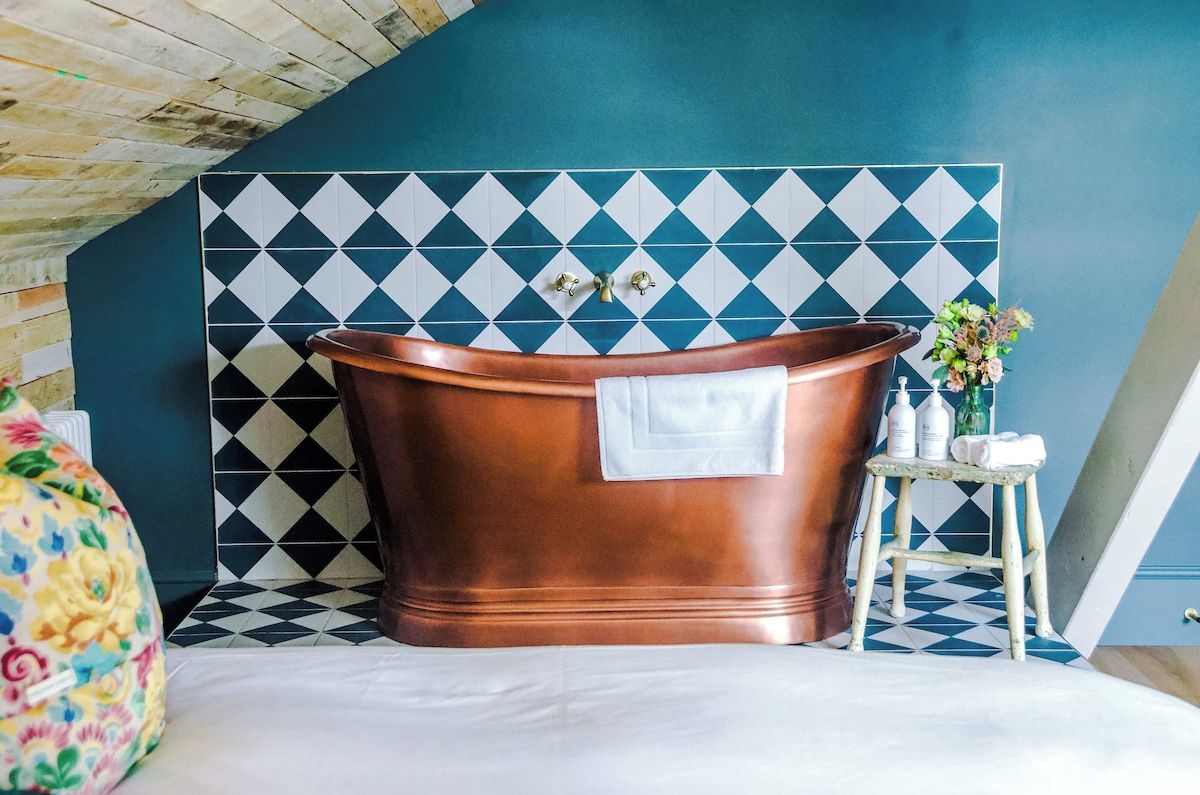 A bathroom with a freestanding copper bathtub, a white towel, and a small stool with toiletries.