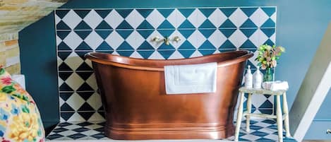 A bathroom with a freestanding copper bathtub, a white towel, and a small stool with toiletries.