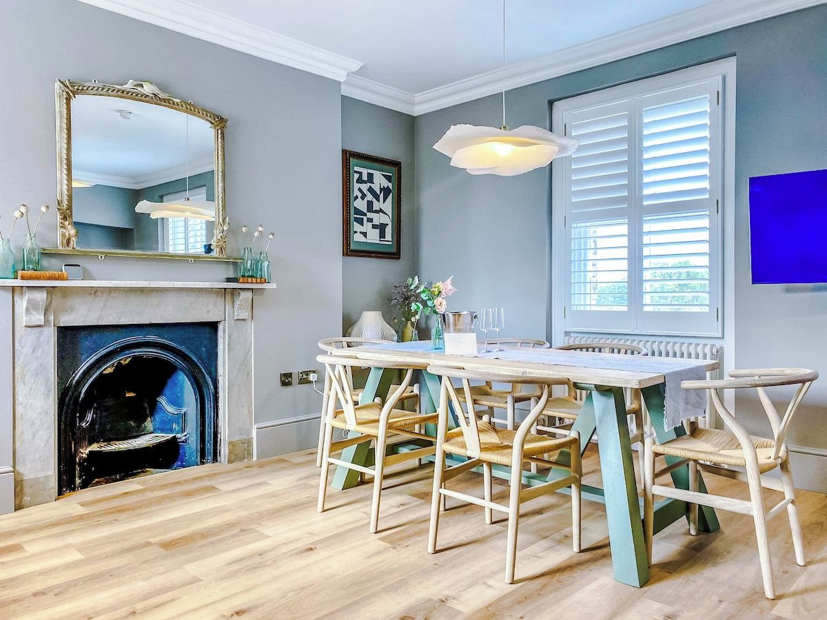 A dining area with a fireplace, a round table with chairs, and a large window with blinds.
