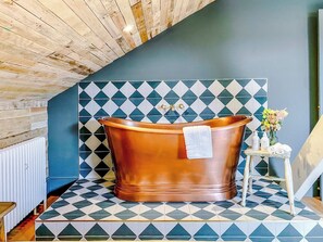 A bathroom with a copper bathtub, a wooden floor, and a blue and white patterned wall.