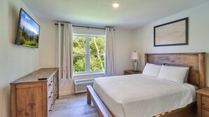 A bedroom with a wooden bed, a nightstand, a dresser, a window with curtains, and a framed picture on the wall.