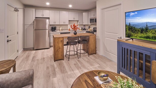 A modern kitchen with white cabinets, a stainless steel refrigerator, and a wooden island with bar stools.