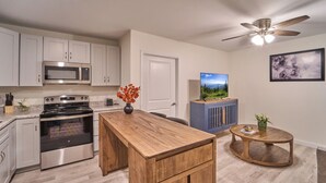 A modern kitchen with stainless steel appliances, a wooden island, and a ceiling fan.