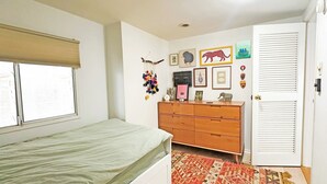 A bedroom with a bed, dresser, wall art, and a door with louvered panels. - Westwood Oasis - 1BR + Loft Office w/ Pool & Gym (Los Angeles)