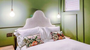 En säng med vita sängkläder och blommig dekorerade kuddar, en sänggavel med ett mönstrat utseende och två hänglampor.