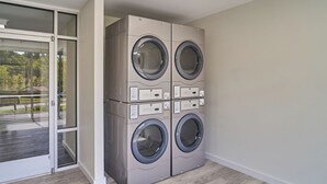 A laundry room with four stacked front-loading washing machines, a glass door leading to an outdoor area, and a wooden floor. - Ruby 314: 2BD | Great LOCATION + Shared Amenities! (Pigeon Forge)