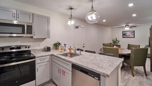 A modern kitchen with stainless steel appliances, a granite countertop, and a dining area with green chairs and a wooden table. - Ruby 314: 2BD | Great LOCATION + Shared Amenities! (Pigeon Forge)
