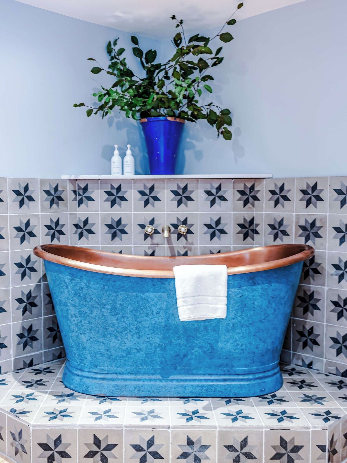 A bathroom with a blue bathtub, a potted plant, and patterned tiles.