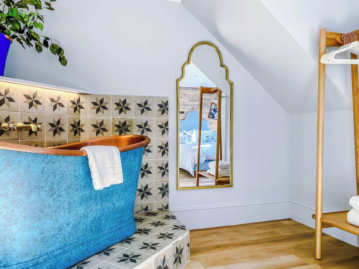 A bathroom with a blue bathtub, a mirror, and a wooden shelf.