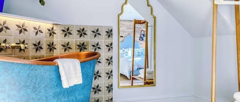 A bathroom with a blue bathtub, a mirror, and a wooden shelf.