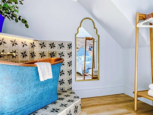 A bathroom with a blue bathtub, a mirror, and a wooden shelf.