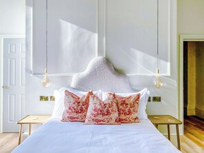 A bedroom with a bed, pillows, a nightstand, and a wall-mounted lamp.