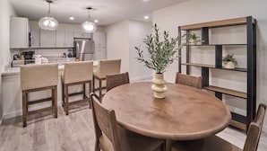Una cocina moderna con armarios blancos, una mesa de comedor de madera e iluminación colgante.