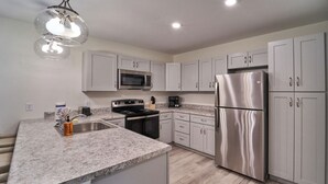 Una cocina moderna con armarios blancos, electrodomésticos de acero inoxidable, encimeras de granito y una isla central con pileta.