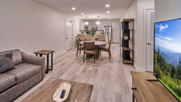 Una sala de estar moderna con un sofá, una mesa de centro y un televisor. Hay un comedor con una mesa y sillas, y una cocina al fondo.