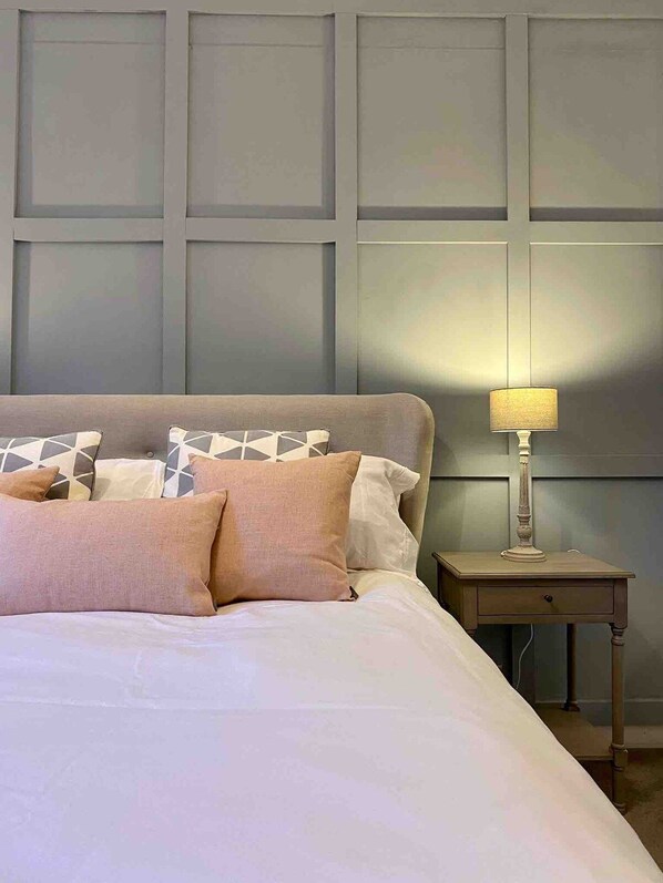 A bed with a patterned headboard, a bedside table with a lamp, and a wall with paneling.