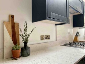 Een keuken met een marmeren aanrecht, een houten snijplank, een potplant en een zwart kastje.