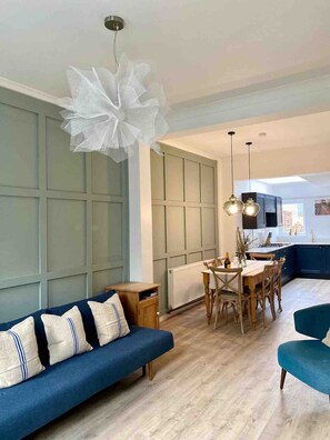 Een moderne woonkamer met een blauwe bank, een houten eettafel en stoelen.