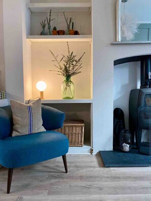 Een woonkamer met een blauwe bank, een lamp, een vaas met planten en een open haard.