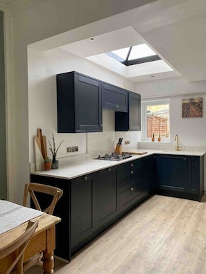A modern kitchen with dark cabinetry, a skylight, and a view of a garden.
