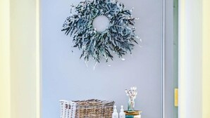 Um corredor com um armário verde, uma cesta de vime e uma coroa decorativa na parede.
